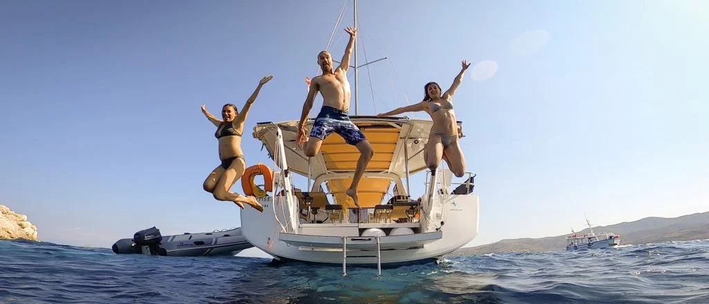 Yacht charter ad Atene: gruppo di persone felici che si tuffano in mare dalla loro barca a vela con skipper