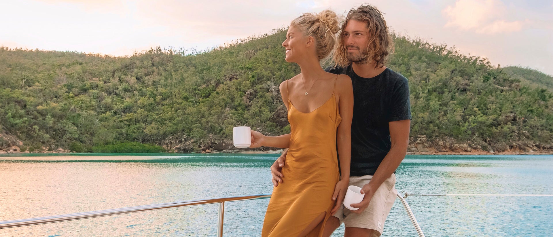 Una pareja en un yate con patrón disfrutando de unas bebidas divisando las Whitsunday 