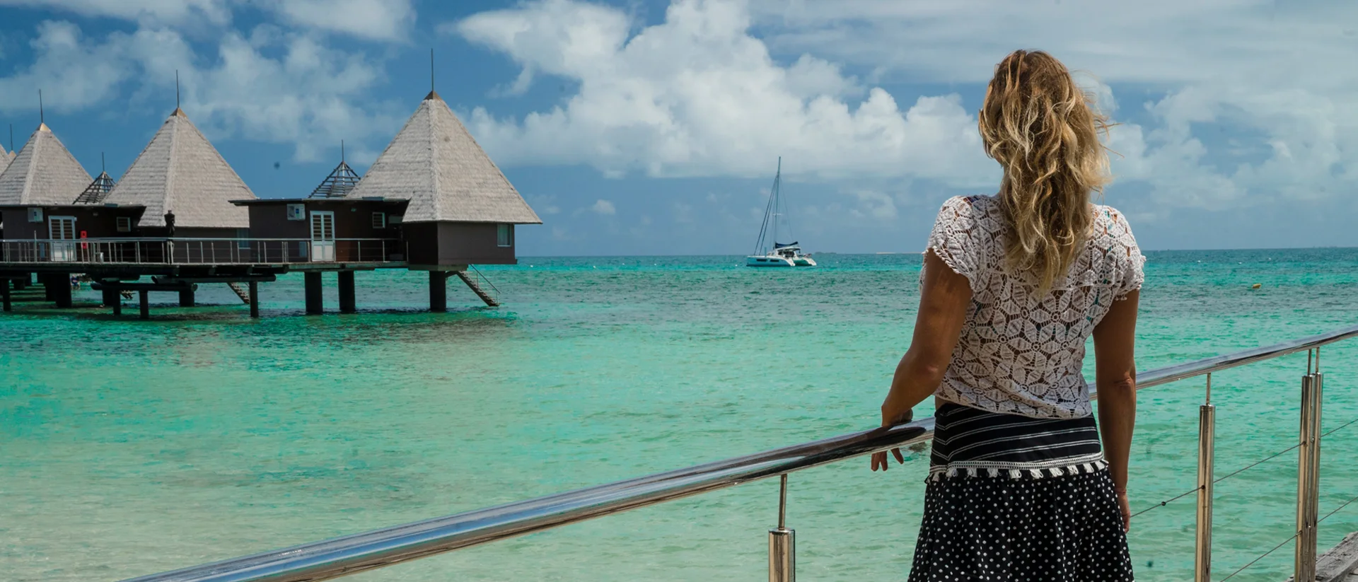 Kvinna tittar på stuga på kristallklar strand och katamaran med skeppare