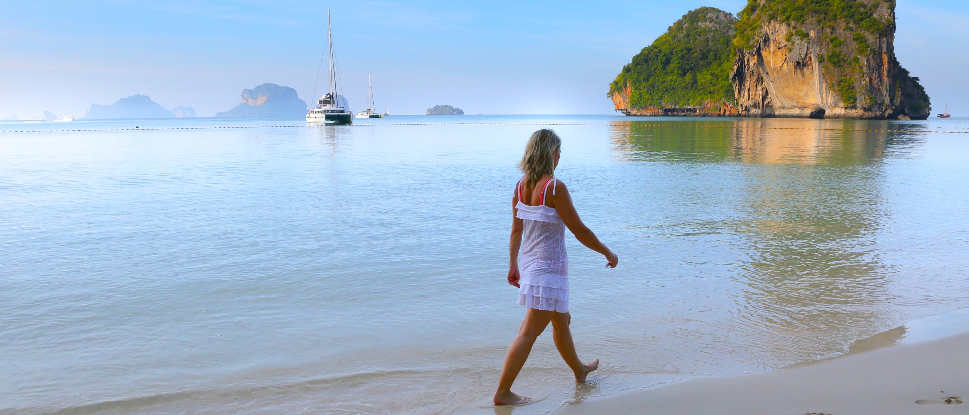 Femme marchant sur une plage sur fond de bateau voguant sur la mer en Thaïlande