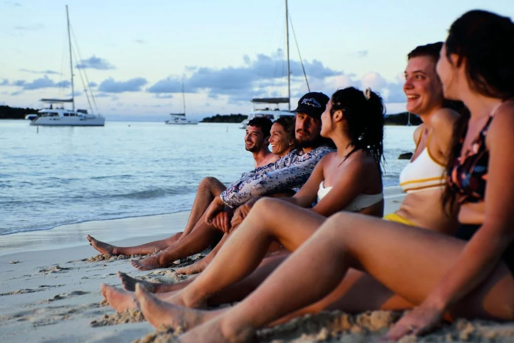 Un grupo disfrutando de la puesta de sol en la playa y un catamarán