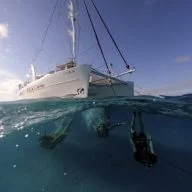 Catamaran yacht charter sailing and people diving in transparent waters