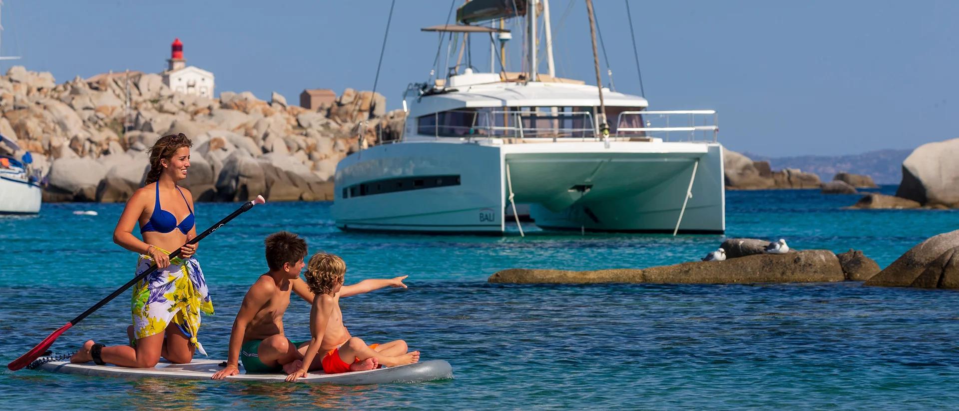 Famiglia in vacanza su un catamarano in Corsica che pratica Paddleboarding