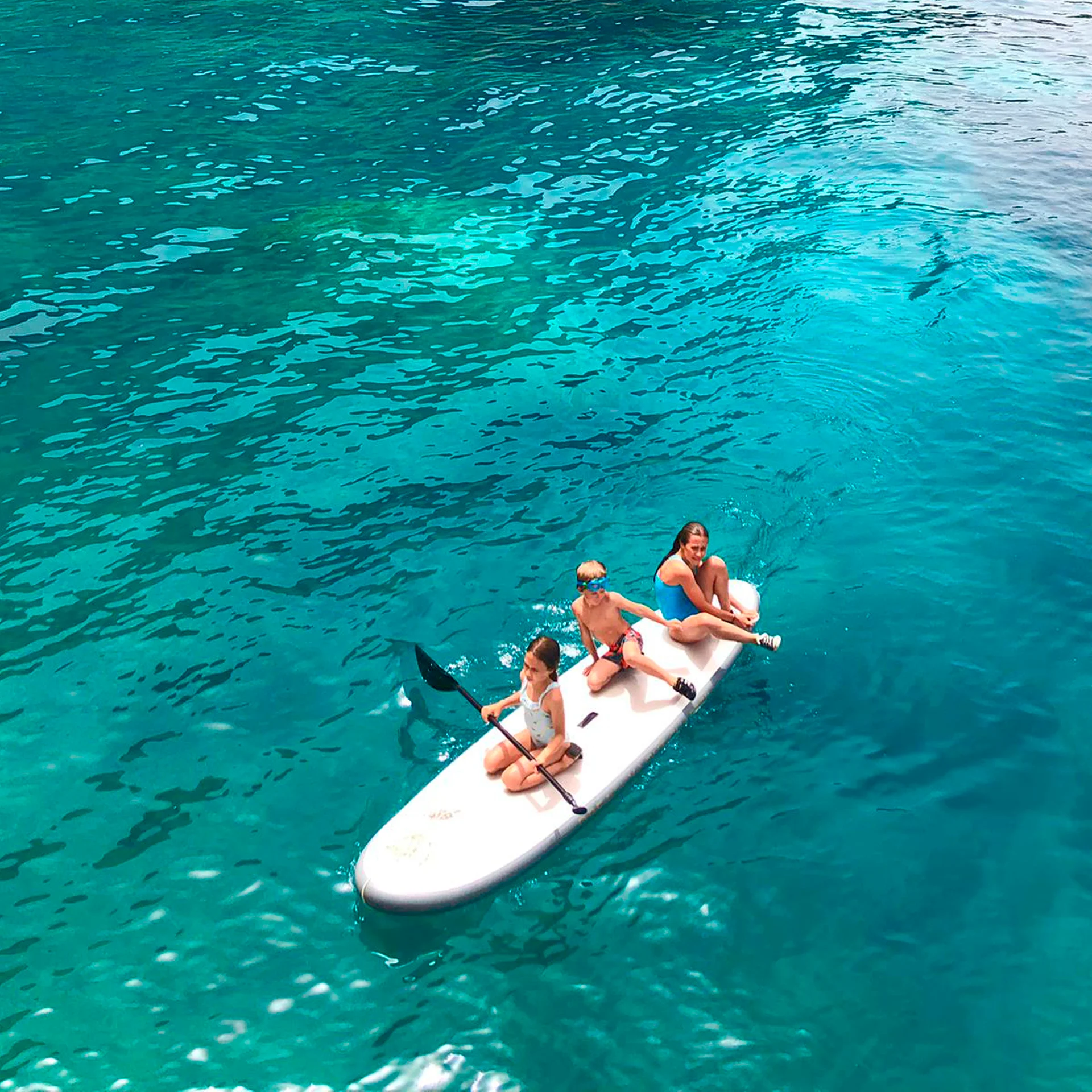 Glückliche Familie beim SUP im kristallklaren Wasser im Sommerurlaub auf Kos