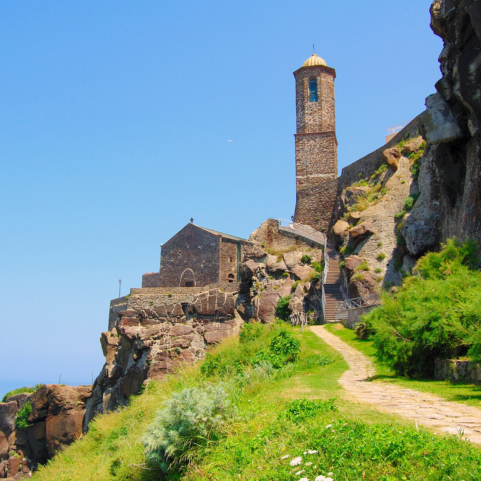 Sentiero nella natura sarda, con scogliera e chiesa