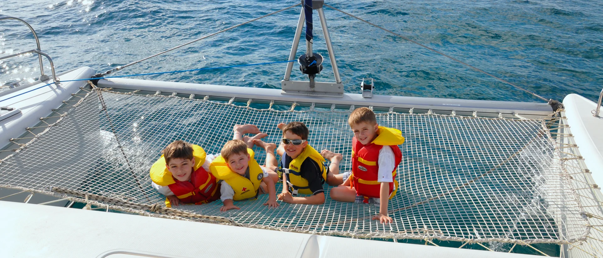 Bambini con occhiali da sole e giubbotti di salvataggio che si godono le vacanze in catamarano