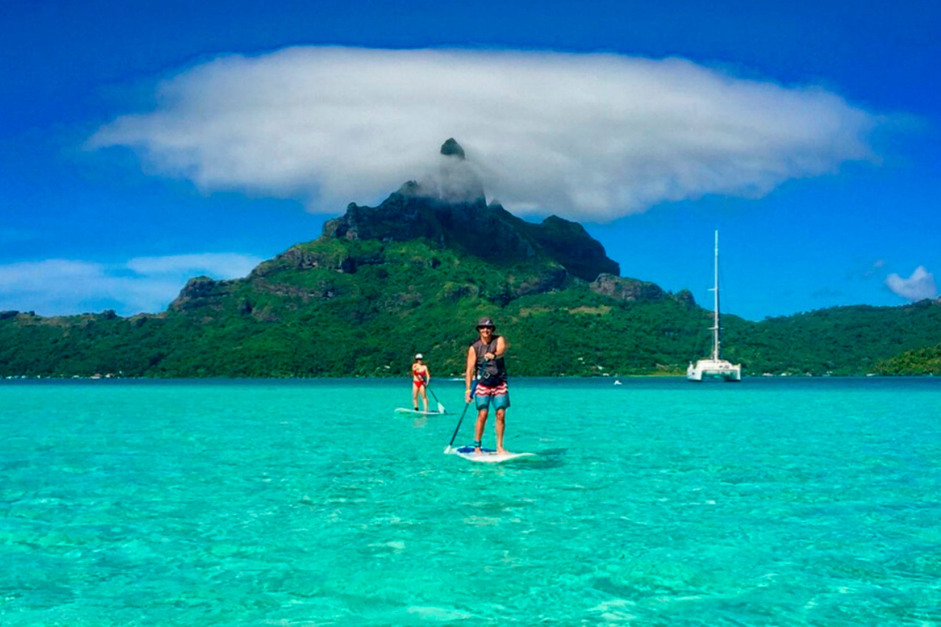 Passagers d'une location de bateau Dream Yacht Charter faisant du paddle sur fond de paysage tahitien