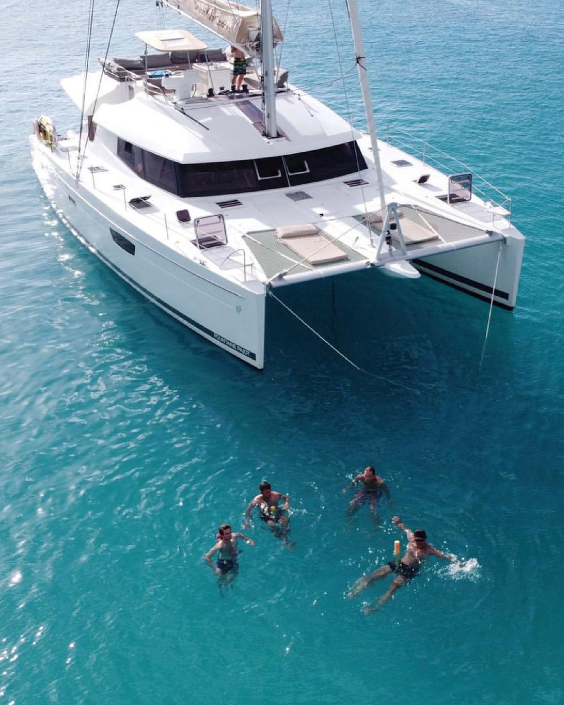 Cabin charter catamaran and people swimming in blue waters