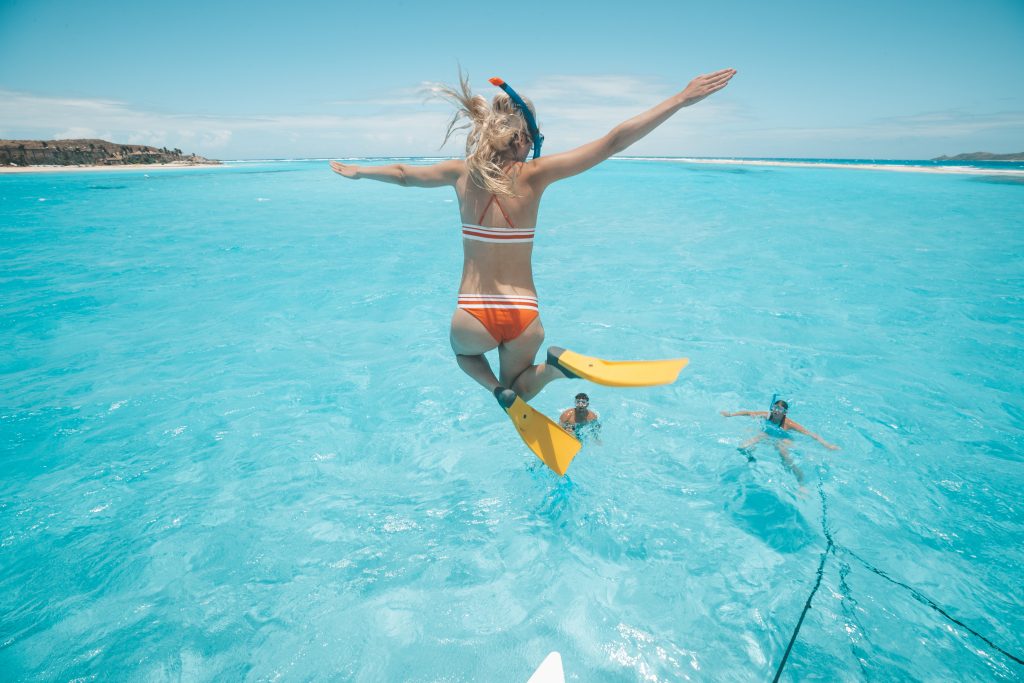 Snorklande flicka hoppar i havet från båtcharter på semestern