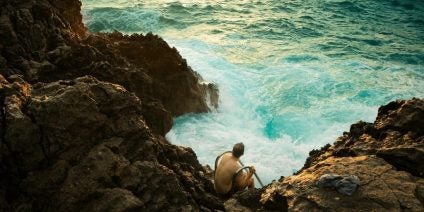man sitting on rocks edge with waves crashing around rocks