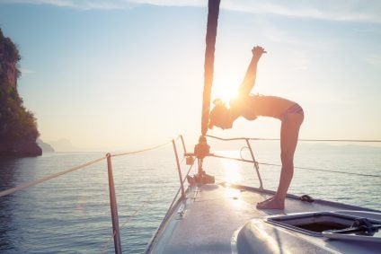 Young lady standing on the bow of yacht and doing exercise at sunrise